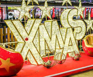 Giant lit letters spelling XMAS with wholesale Christmas lights, surrounded by giant glitter star props, and two Christmas ornament chairs inside commercial shopping mall